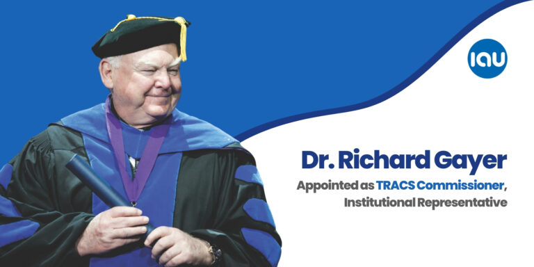 Dr. Richard Gayer, Chief Academic Officer of IAU, appointed as TRACS Commissioner and Institutional Representative; standing in academic regalia beside blue background featuring IAU logo and text announcing his leadership role with the Transnational Association of Christian Colleges and Schools.